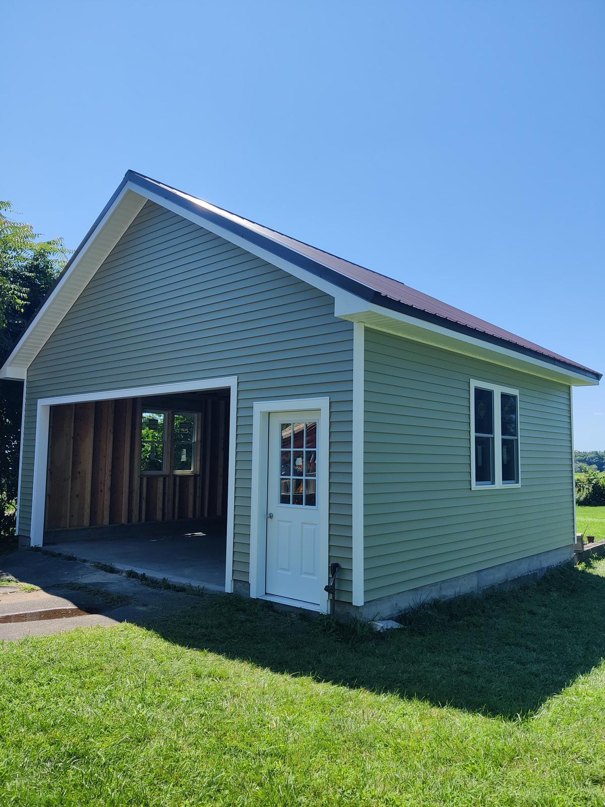 Light green single-car garage with white trim and a dark metal roof — a 20×24 one-bay single-level garage