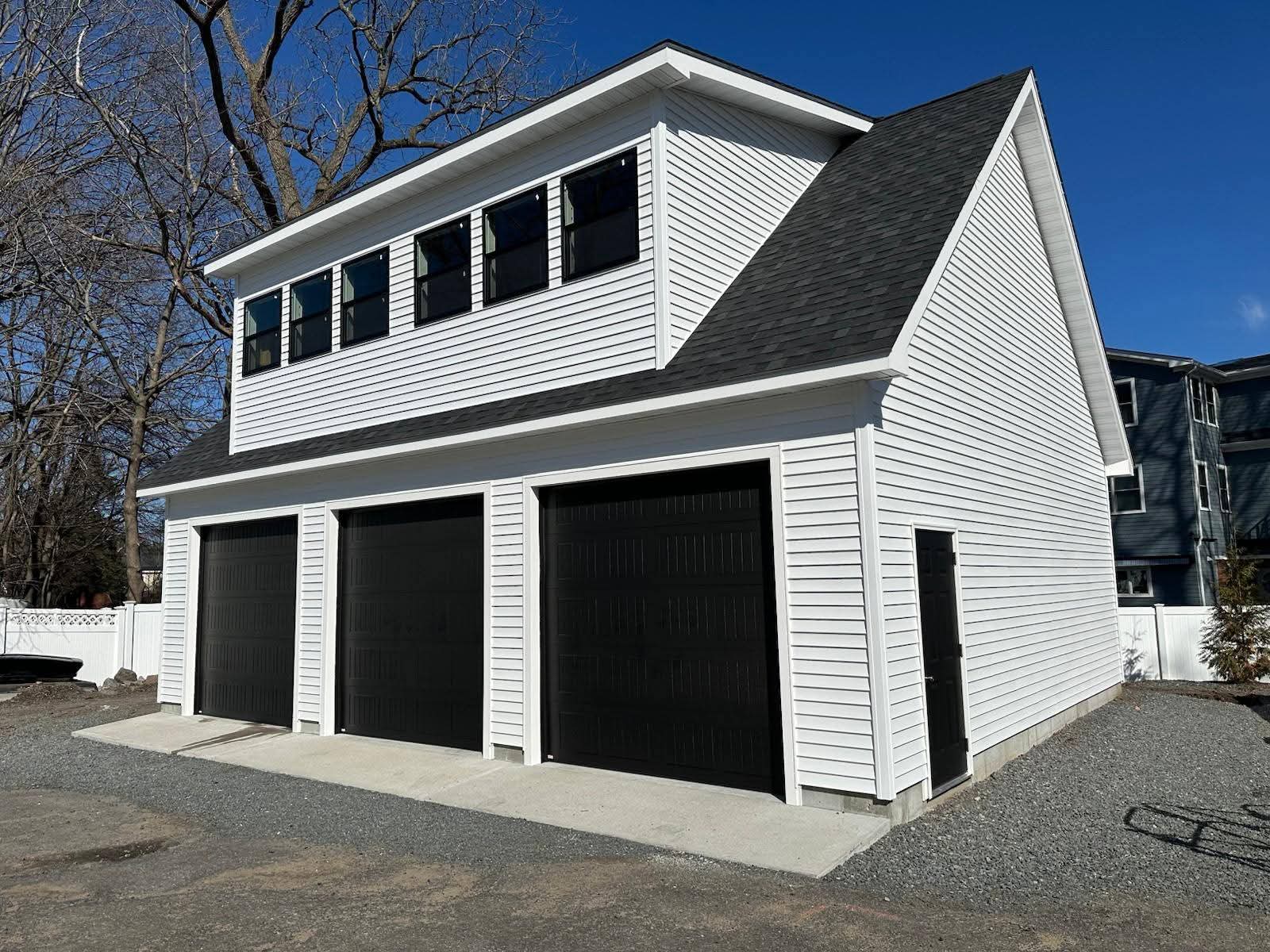 White two-story garage with three black doors on the eave side — three bays entered from the long side, 24×36