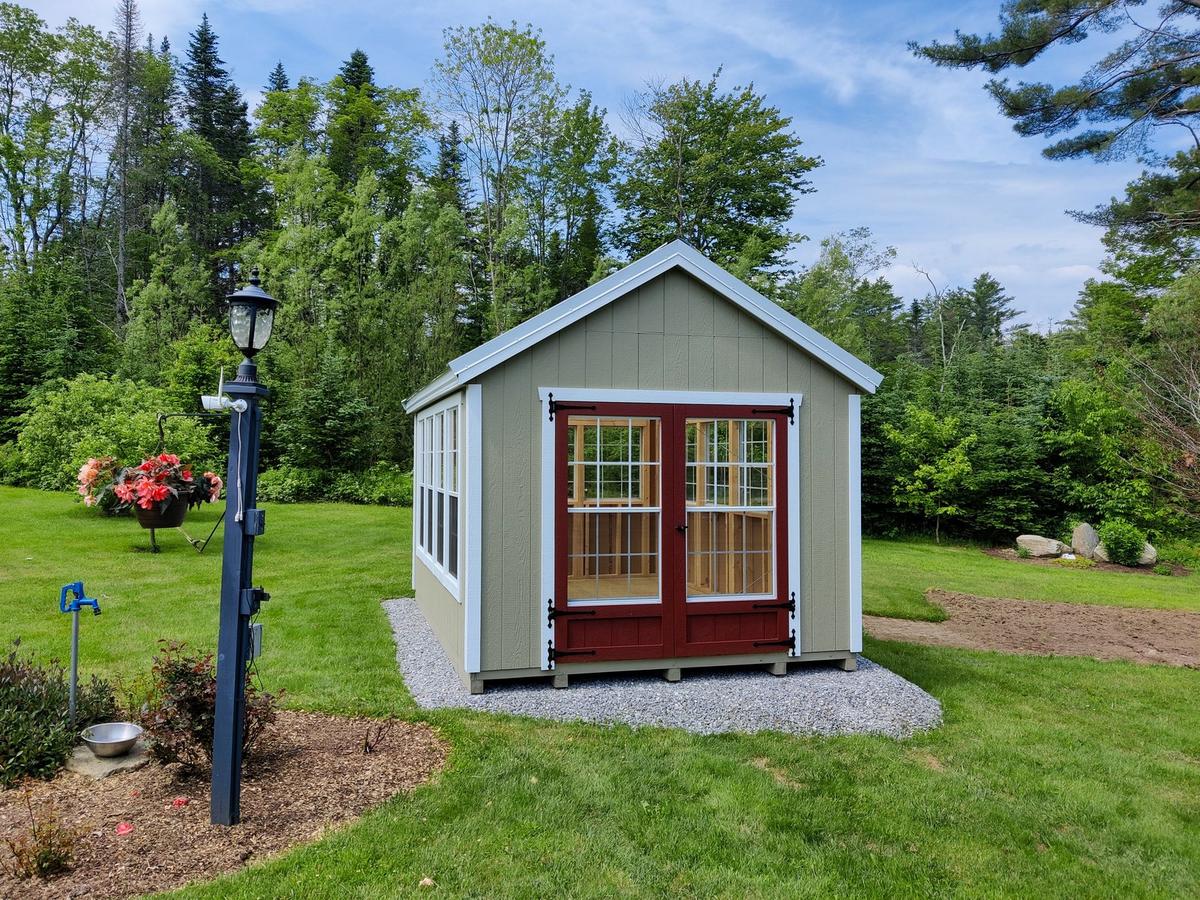 Keystone greenhouse sitting on a gravel pad in a large landscaped backyard