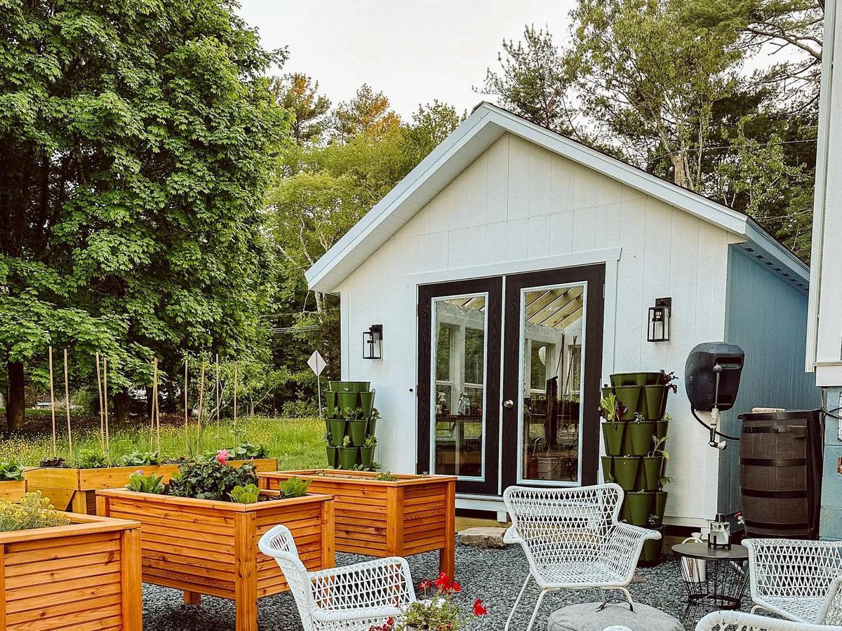 New england greenhouse in a backyard next to a garden